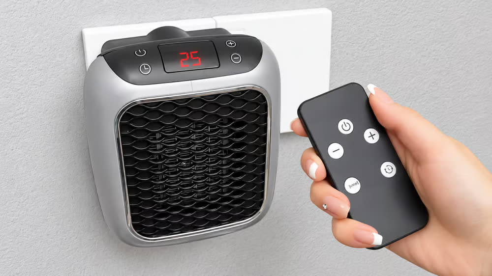 Hand holding the RapidHeat remote control next to the wall-mounted heater showing 25 on its display